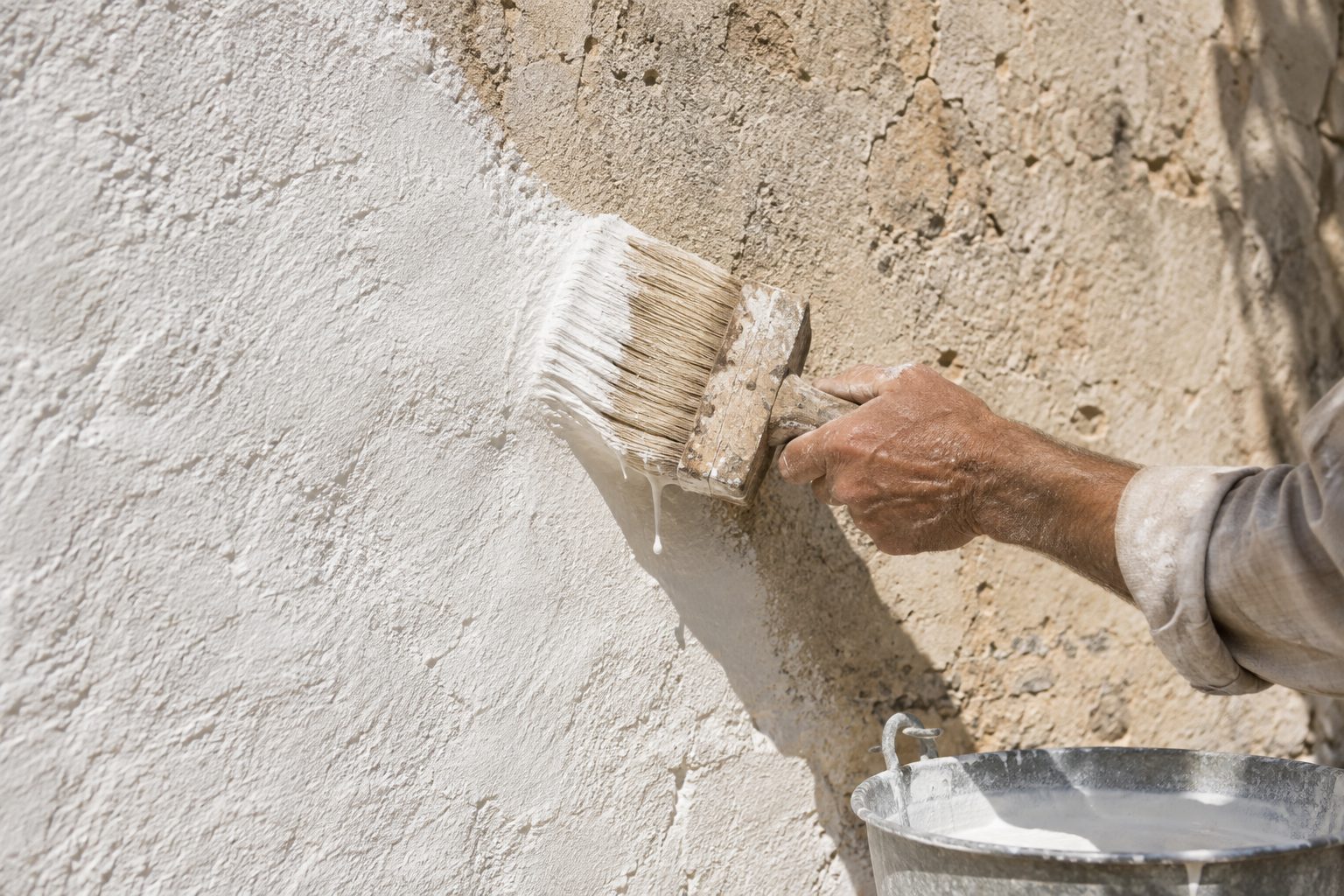 Una pennellessa stende il latte di calce su un muro spesso, in pieno sole